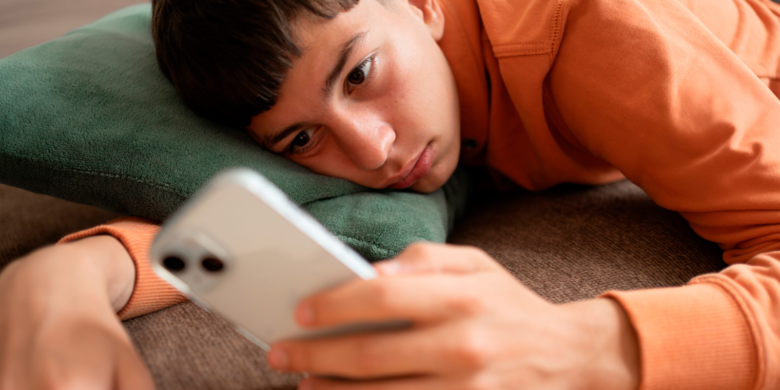 Adolescente absorto en el celular, recostado en el sofá